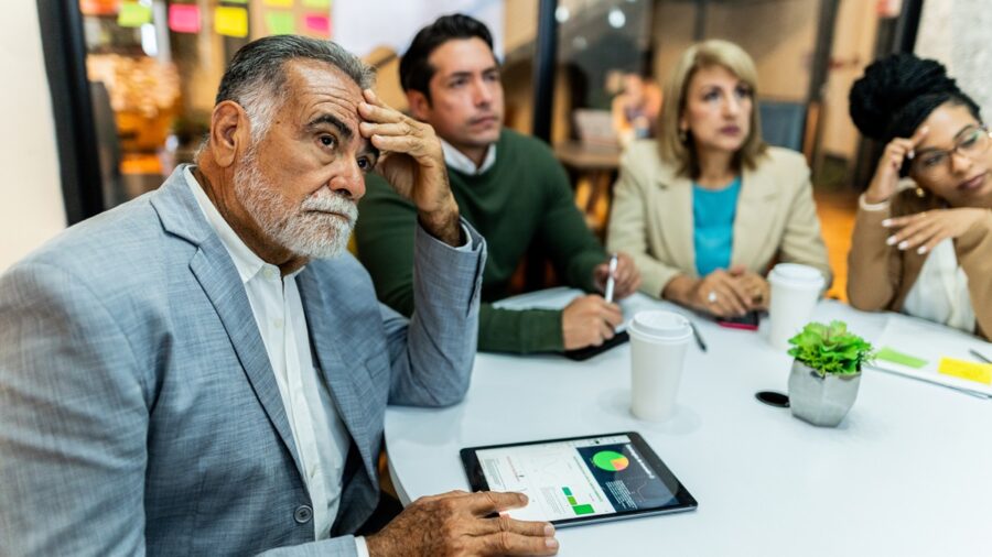 Worried Senior Businessman Listening Presentation With Coworkers During Business Meeting At Office